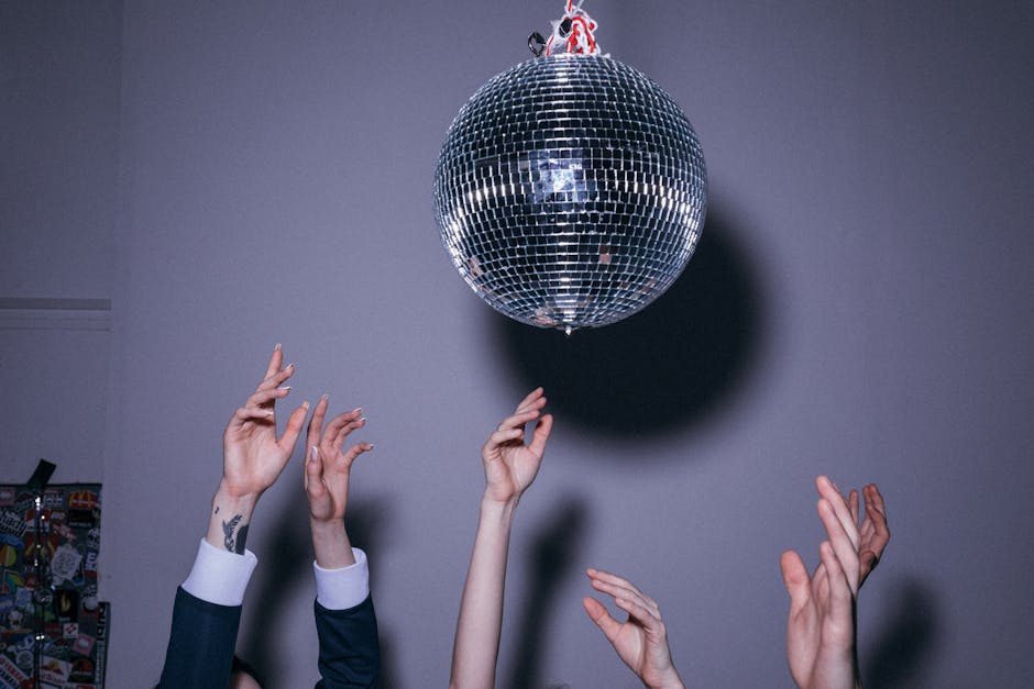 People reaching for a disco ball, capturing the essence of a lively indoor dance party.